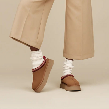 Person wearing a brown shearling jacket and beige pants on a beige background