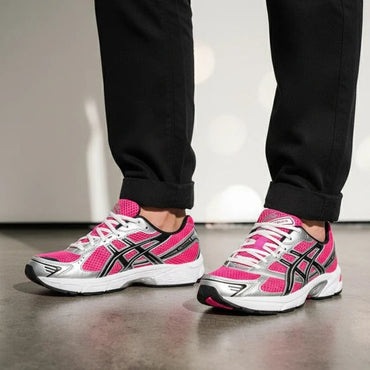 Pink and white running shoes with black accents worn by a person in black pants.
