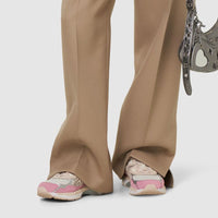 Person wearing beige wide-leg pants holding a decorative handbag on a white background