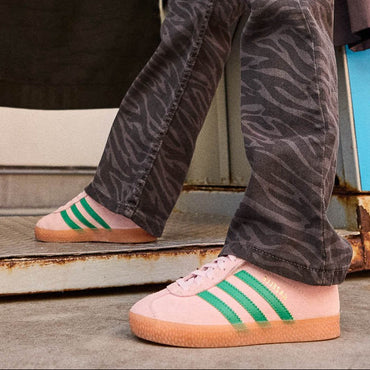 Person wearing pink Adidas sneakers with green stripes on a metal surface.