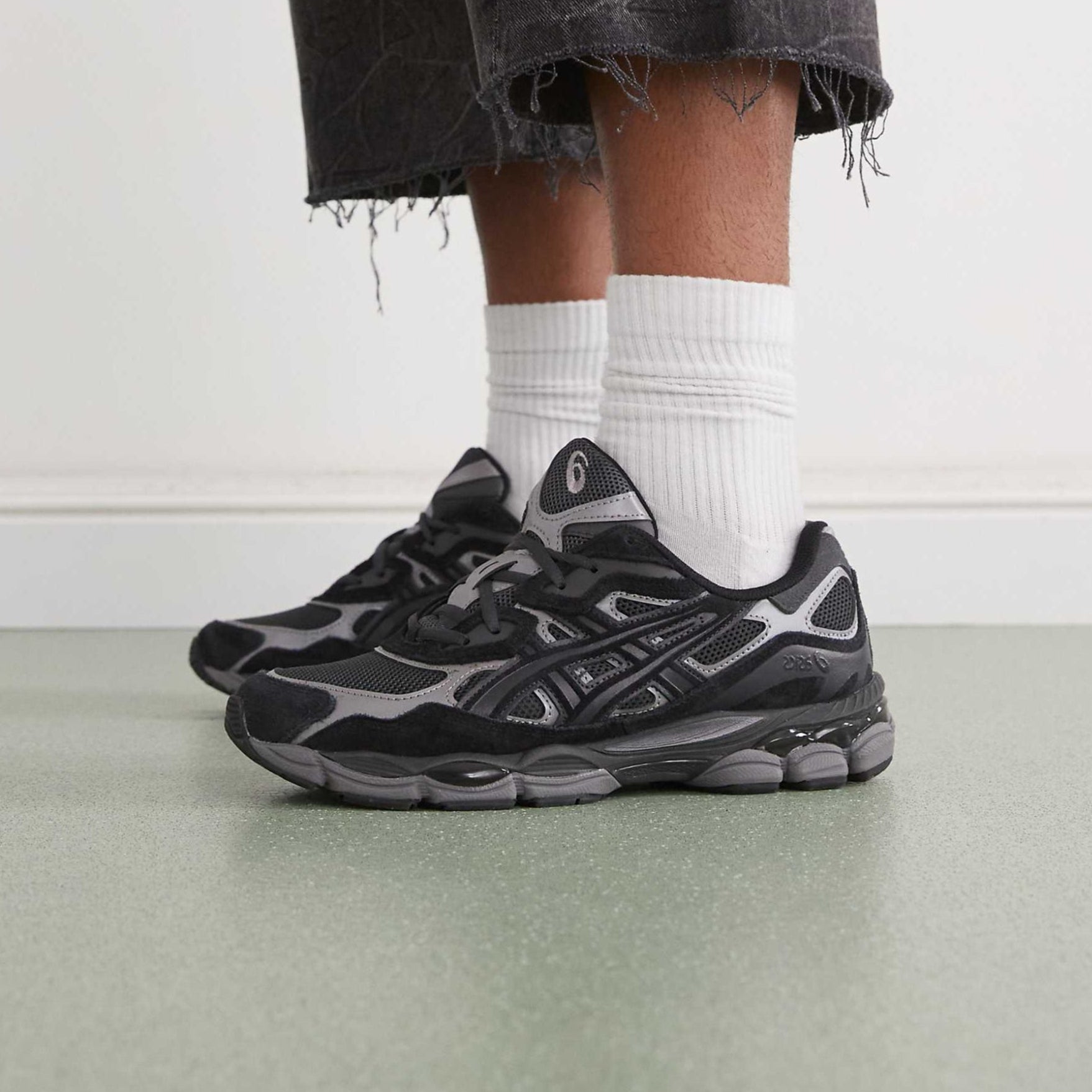 Person wearing black and gray sneakers with white socks on a light background