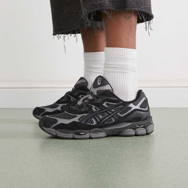 Person wearing black and gray sneakers with white socks on a light background