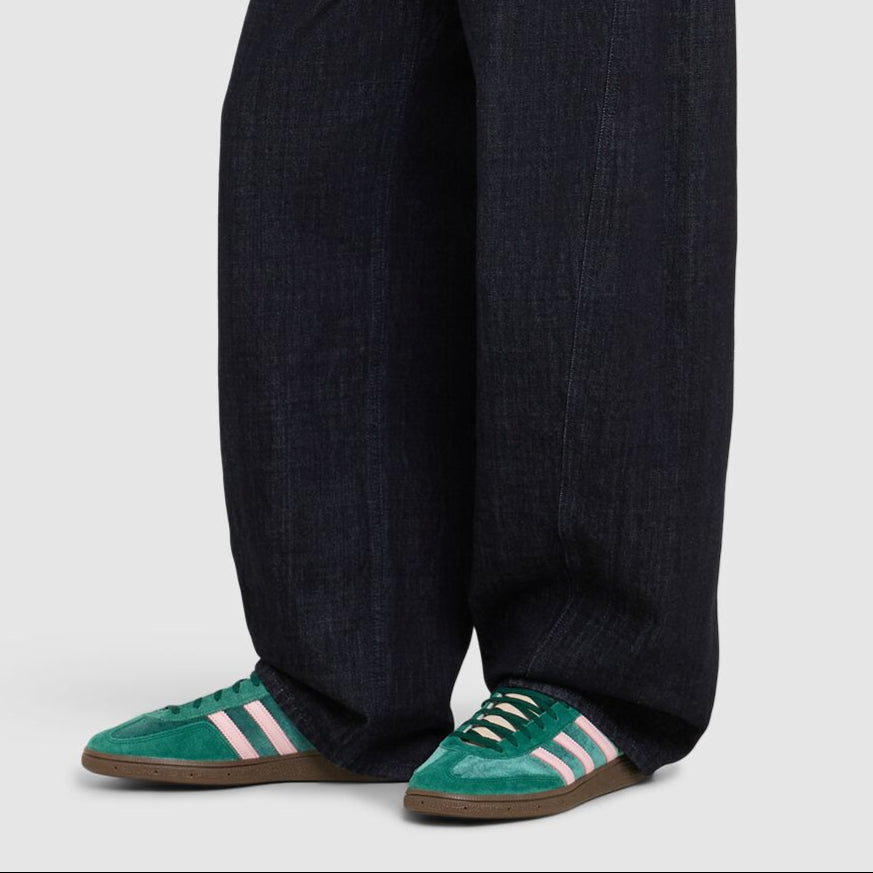 Person wearing dark wide-leg jeans and green shoes on a white background