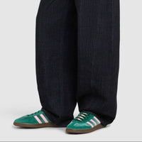 Person wearing dark wide-leg jeans and green shoes on a white background