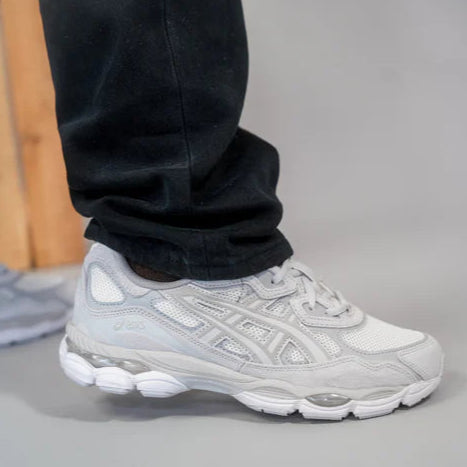Gray athletic shoe worn with black pants on a neutral background