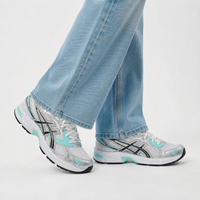 White and gray sneakers with turquoise accents worn with light blue jeans on a white background