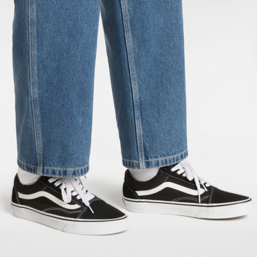 Black and white Vans Old Skool sneakers worn with blue jeans on a clean white background.