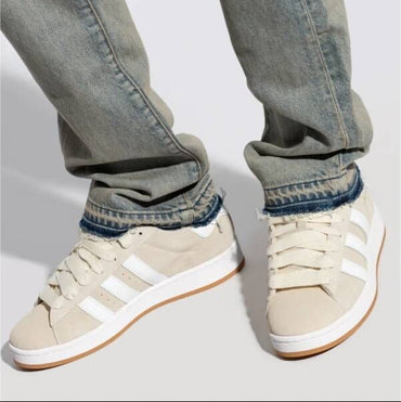 Beige sneakers with white stripes worn with rolled-up jeans on a light gray background