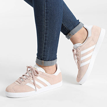 Person wearing light pink Adidas sneakers with white stripes on a light background