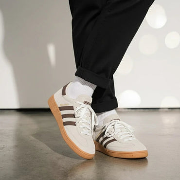 White sneakers with brown soles and stripes worn indoors on a light wooden floor.