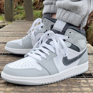 Gray and white sneakers worn on a wooden platform with a natural background