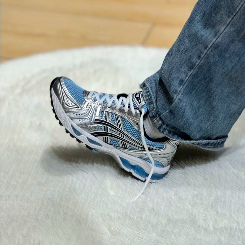 Person wearing a blue and white sneaker on a white surface with a wooden floor in the background