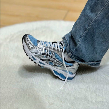 Person wearing a blue and white sneaker on a white surface with a wooden floor in the background