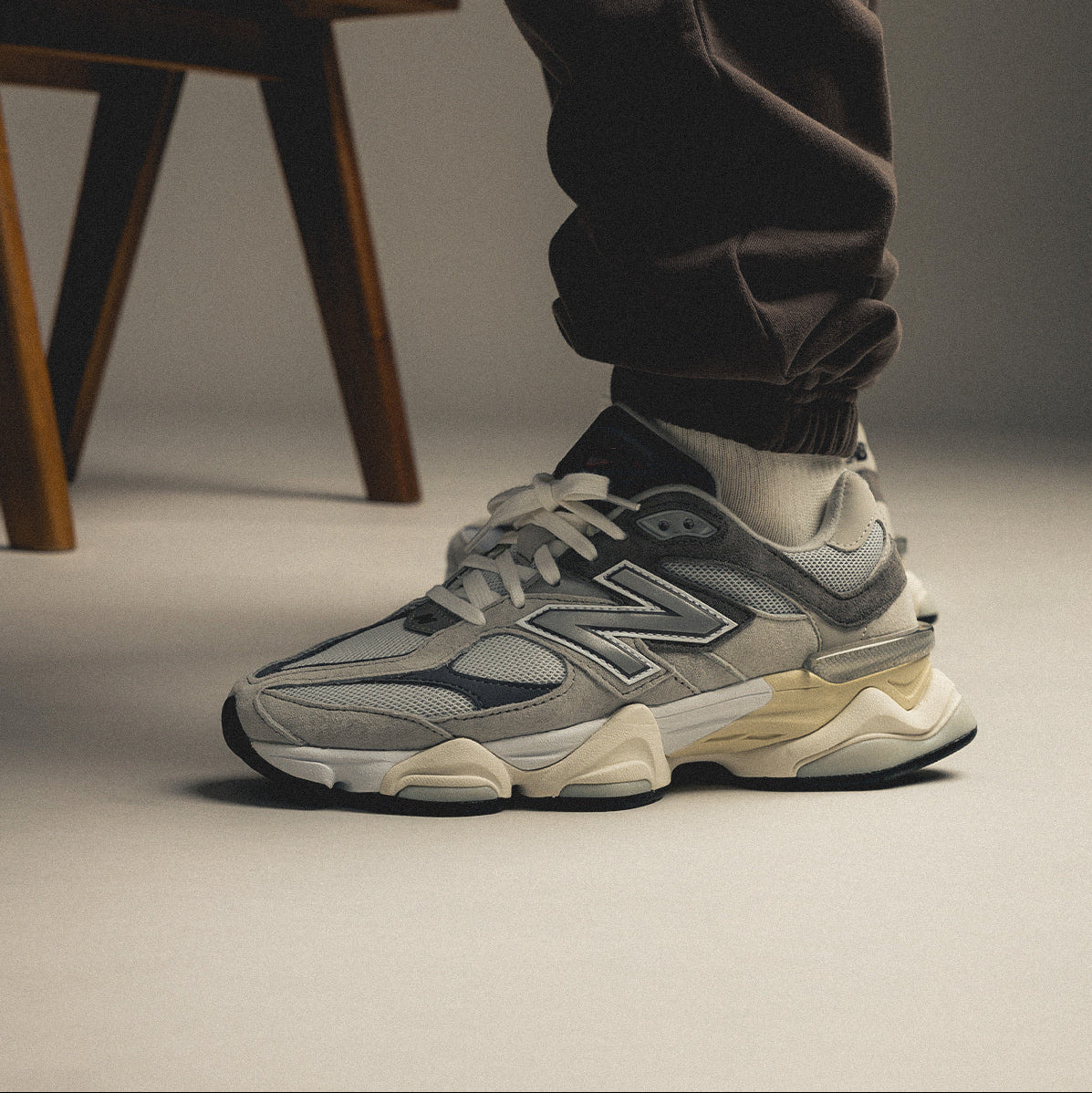 Gray New Balance sneakers worn with dark pants on a neutral background