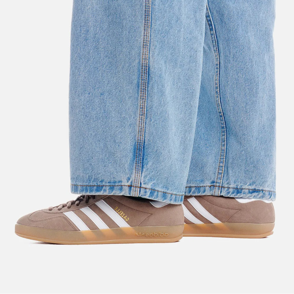 Beige Adidas sneakers with white stripes worn with light blue jeans on a white background