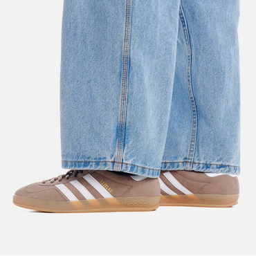 Beige Adidas sneakers with white stripes worn with light blue jeans on a white background