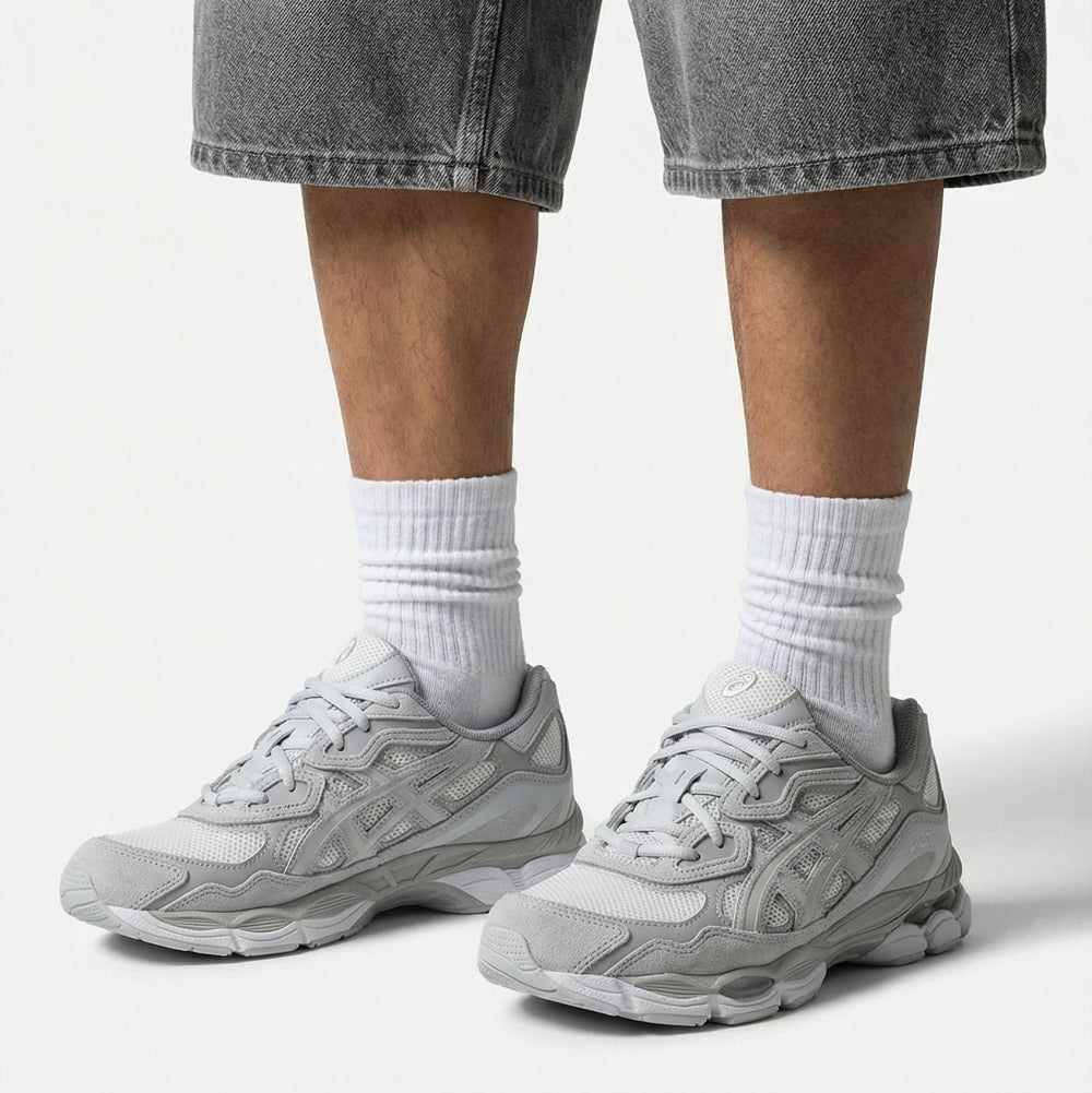 Person wearing gray sneakers, white socks, and gray denim shorts on a light background
