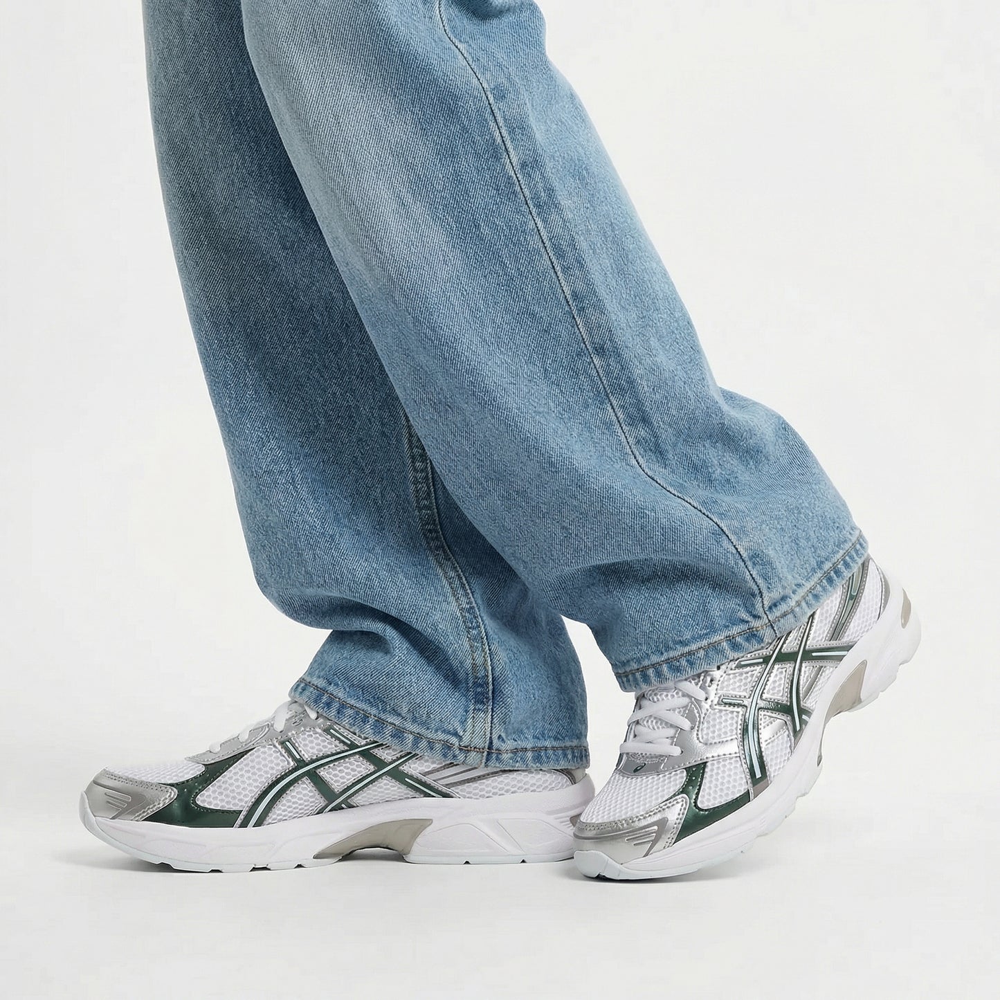 Person wearing blue jeans and white sneakers with green accents on a light gray background