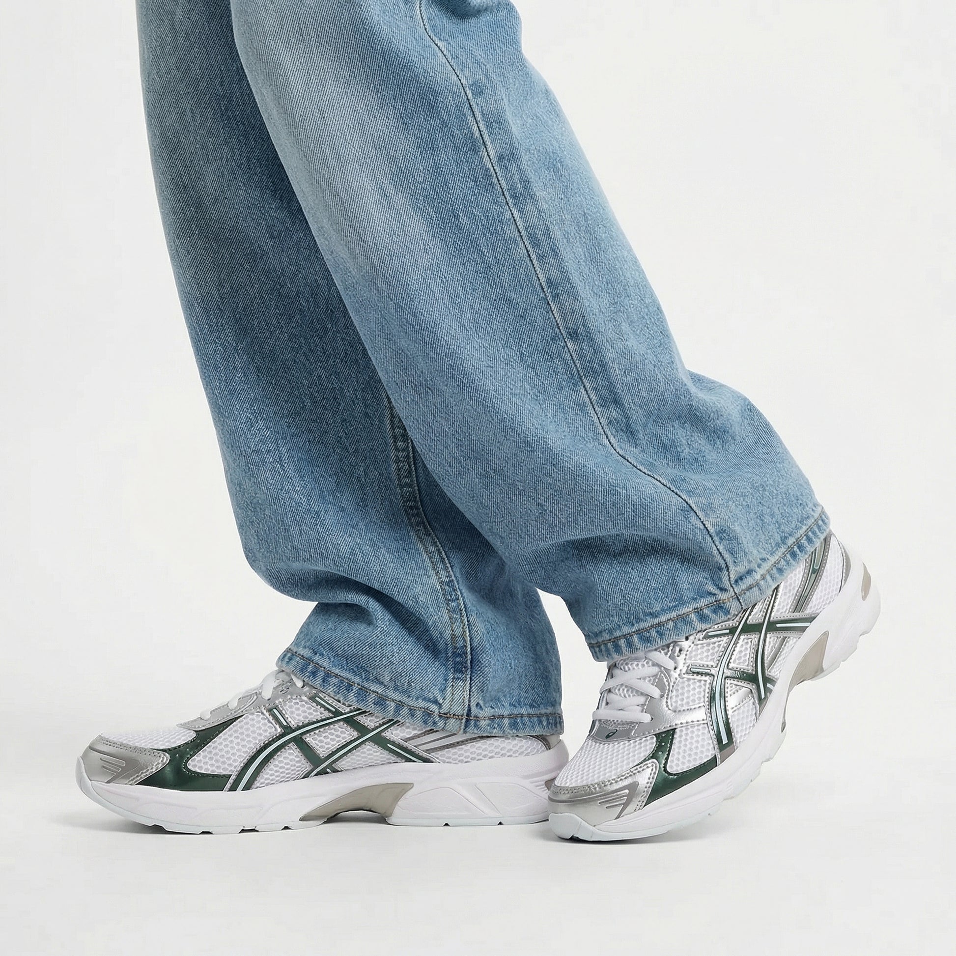 Person wearing blue jeans and white sneakers with green accents on a light gray background