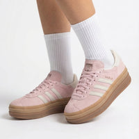 Pink sneakers with white stripes worn with white socks on a light gray background