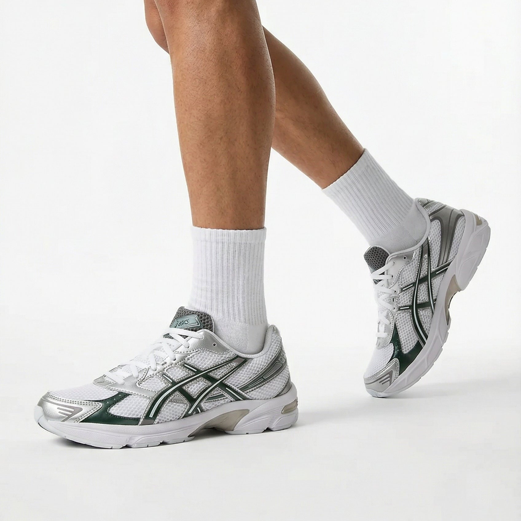 Person wearing white sneakers with black accents on a light gray background