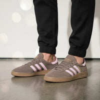 Person wearing brown Adidas sneakers with pink stripes on a reflective floor.