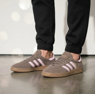 Person wearing brown Adidas sneakers with pink stripes on a reflective floor.