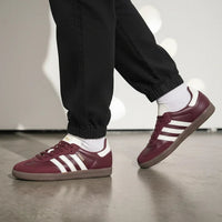 Maroon off-white Adidas sneakers with white stripes worn indoors on a neutral background