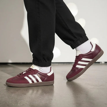 Maroon off-white Adidas sneakers with white stripes worn indoors on a neutral background