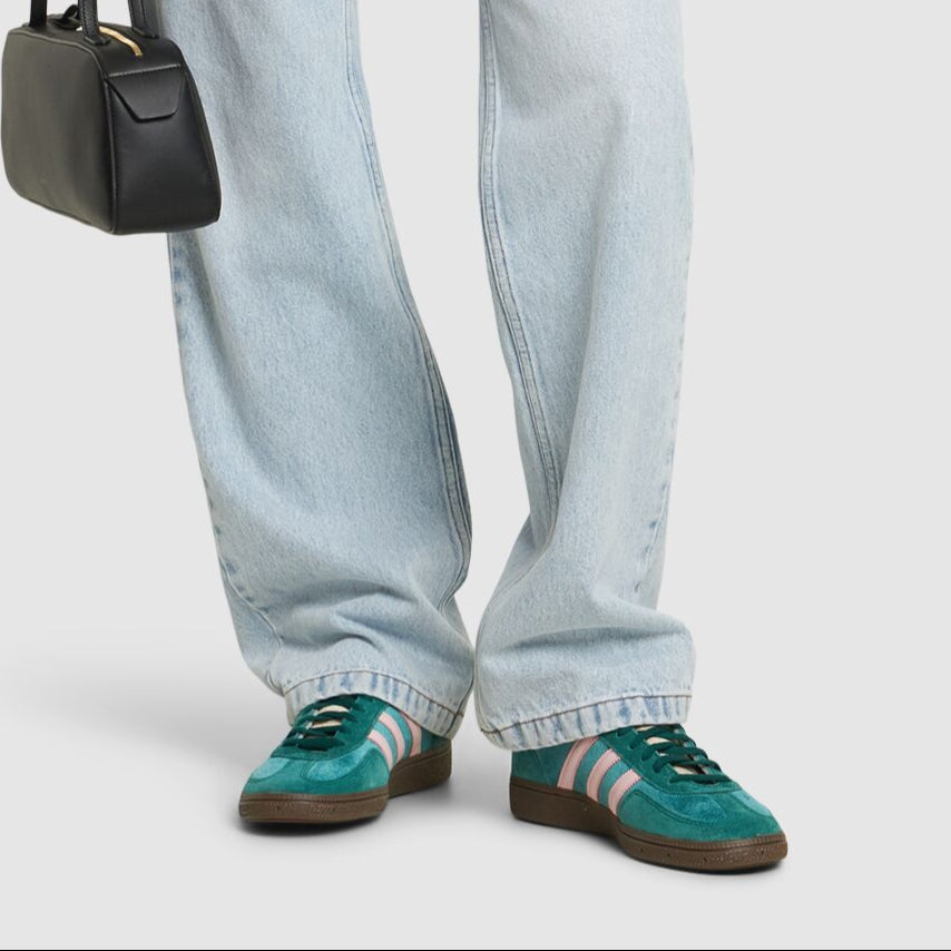 Person wearing a beige blazer, light blue jeans, and green sneakers holding a black handbag.