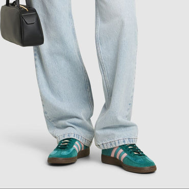 Person wearing a beige blazer, light blue jeans, and green sneakers holding a black handbag.