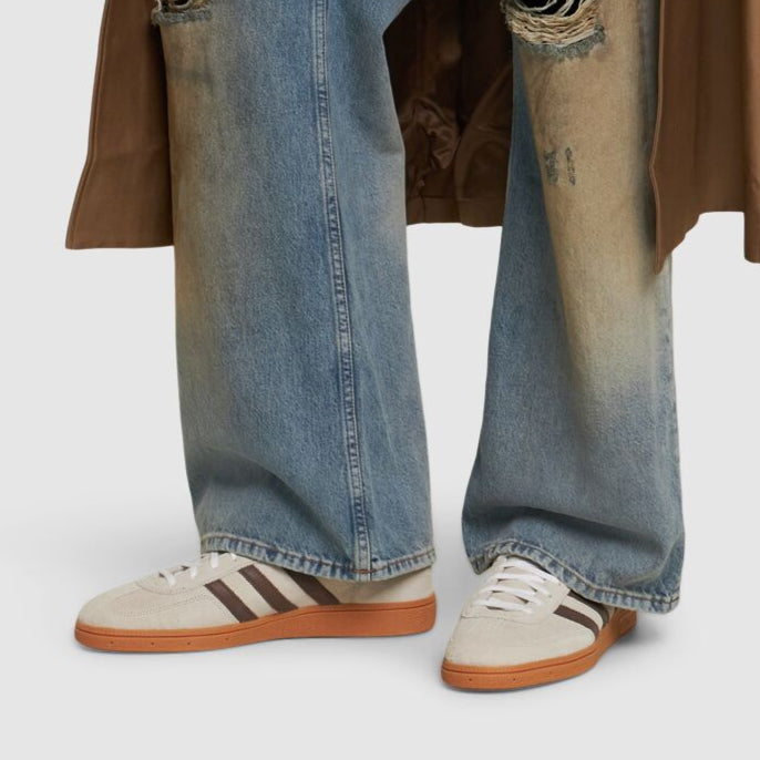 Person wearing blue jeans and white sneakers with brown soles on a light gray background